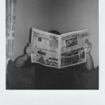 Person reading a newspaper at home in a vintage black and white style.