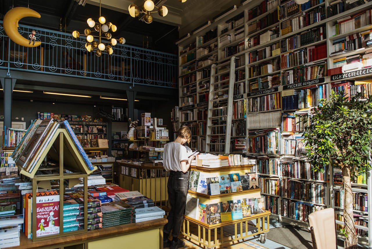 A person enjoys a book in a sunlit, cozy bookstore filled with a variety of books.