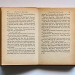 Vintage book opened to pages 76-77, displaying classic literature text in soft lighting.